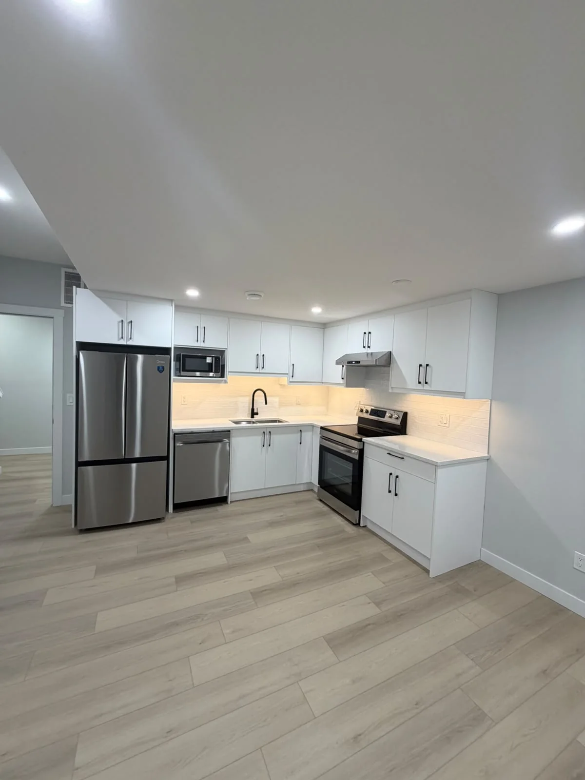 Finished basement kitchen with white cabinets and stainless appliances