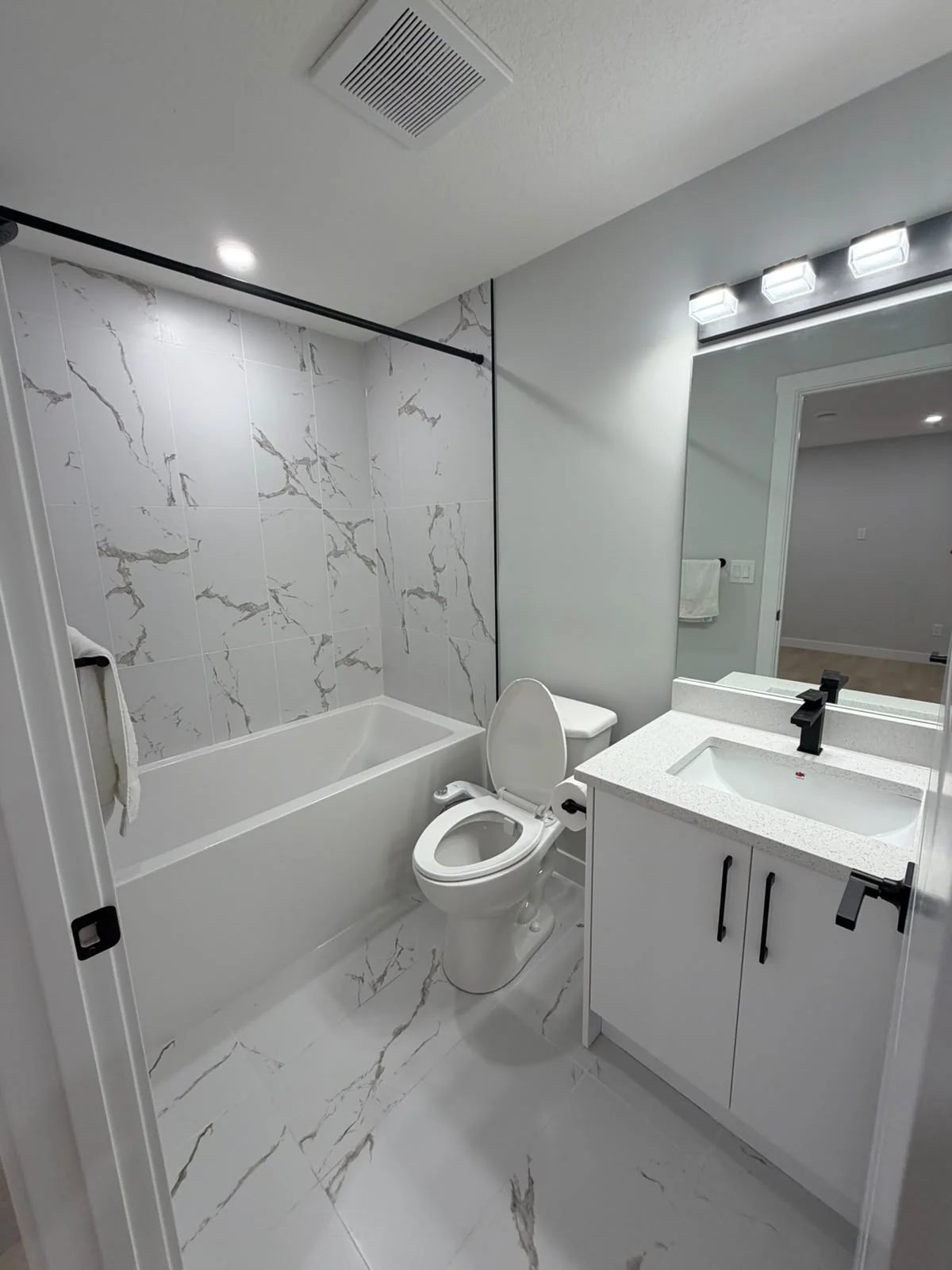 Modern bathroom renovation with marble-look tile and black fixtures